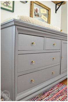 a gray dresser sitting on top of a wooden floor next to a wall with pictures above it