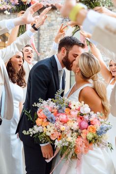 a bride and groom are surrounded by confetti as they kiss in front of their wedding party