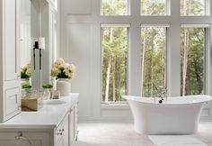 a white bathroom with a tub, sink and large windows in it's walls