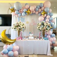 a table topped with balloons and flowers next to a white table cloth covered in blue, pink and gold balloons