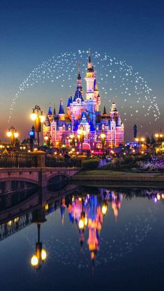 the disneyland castle is lit up at night with fireworks in the sky above it and reflecting in the water