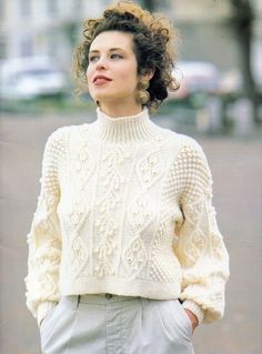 a woman with curly hair wearing a white sweater and gray pants standing in the street