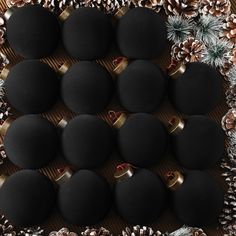 twelve black christmas baubles with gold rings and pine cones in the middle, surrounded by evergreen cones