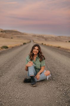 a woman sitting in the middle of an empty road with her legs crossed and smiling