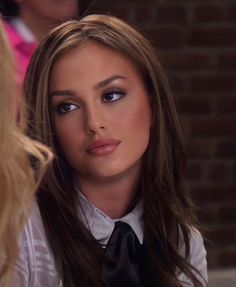 a woman with long brown hair wearing a white shirt and black tie looking into the camera