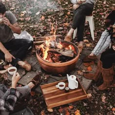 group of people sitting around a fire pit with cups of coffee in front of them