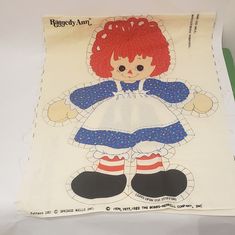 a paper doll with red hair and blue dress on it's chest sitting on a table