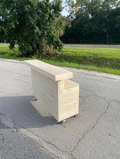 a wooden box sitting on the side of a road next to a field and trees