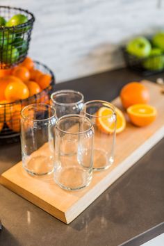 three glasses on a cutting board with oranges and apples in the background