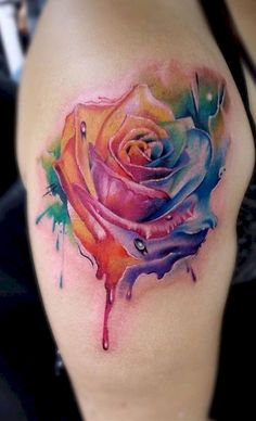 a colorful rose tattoo on the side of a woman's arm and shoulder, with watercolor splashes