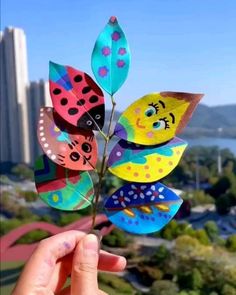 a person holding up a paper flower with ladybugs on it in front of a cityscape