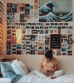 a woman sitting on top of a bed in front of a wall covered with pictures