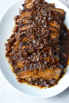 a white plate topped with meat covered in gravy on top of a table