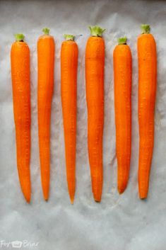 five carrots are lined up in a row on a piece of parchmented paper