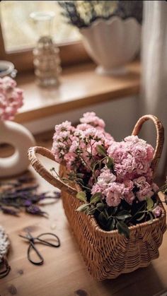 pink flowers in a wicker basket sitting on a table next to scissors and other crafting supplies