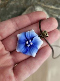 a hand holding a small blue flower on a string