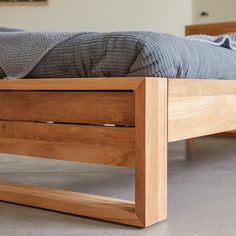 a wooden bed frame sitting on top of a cement floor next to a gray blanket