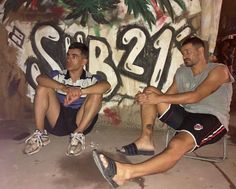 two men sitting next to each other in front of graffiti