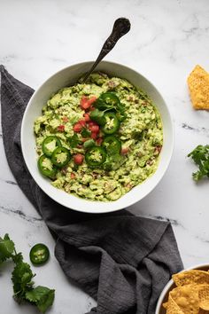 a white bowl filled with guacamole surrounded by tortilla chips and cilantro