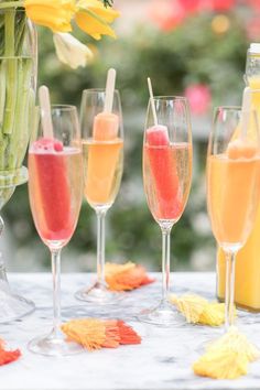 there are many different types of drinks in glasses on the table with flowers around them