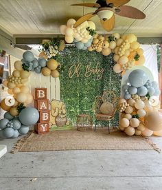 an outdoor baby shower with balloons and greenery on the wall, along with other decorations