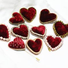 several red and gold heart shaped brooches with pearls on them sitting on a white surface