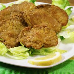 some fried food on a white plate with lettuce and lemon wedges