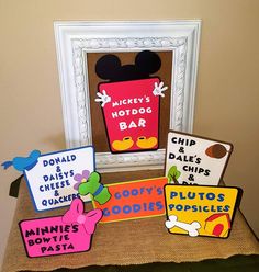 mickey mouse's hot dog bar sign and other signs on display in front of a frame