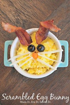 a bowl filled with scrambled eggs and bacon on top of a wooden table next to an orange slice