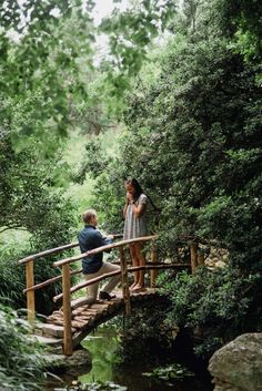 a man and woman standing on a bridge in the woods