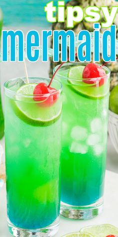 two glasses filled with blue and green liquid on top of a table next to fruit