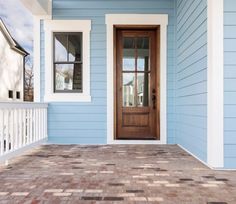 a blue house with a wooden door and white trim on the front porch, next to a brick walkway