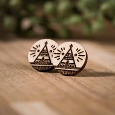 pair of wooden earrings with mountains and trees on them sitting on a wood table top