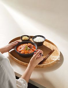 a woman is holding chopsticks over a bowl of food on a wooden tray