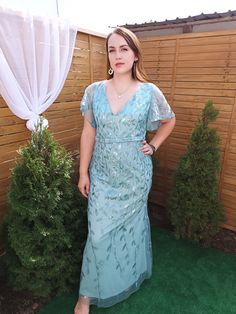 a woman standing in front of a wooden fence wearing a blue dress with sheer sleeves