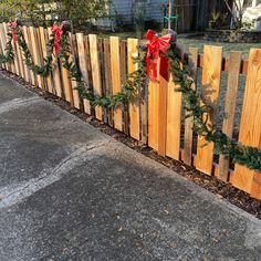 a wooden fence decorated with christmas garlands and bows on the top, next to a sidewalk