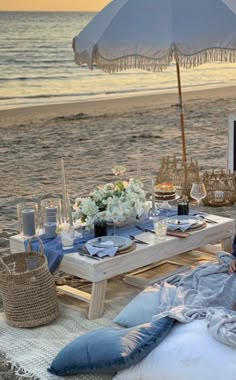 a table set up on the beach with an umbrella over it and flowers in vases