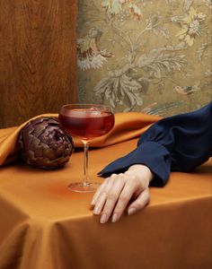 a woman sitting at a table with a glass of wine and an artichoke