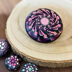 three painted rocks sitting on top of a wooden plate next to some wood slices and flowers