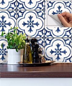 a hand is holding a bottle and some plants on a counter top in front of a blue and white tile wall