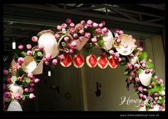 a decorated archway with pink flowers and straw hats hanging from it's sides in front of a mirror