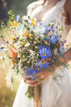 a bride holding a bouquet of wildflowers and daisies in her hands,