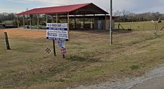 a sign in the middle of a grassy field with a red roof on top of it