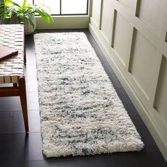 a white rug on the floor in front of a window with a potted plant next to it