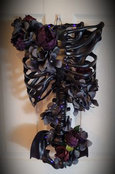 a metal sculpture with flowers and leaves on it's side hanging from the wall