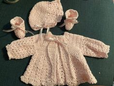 a crocheted baby outfit and booties on a green surface with other items