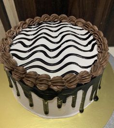 a white and black cake sitting on top of a gold plated platter next to a wooden wall