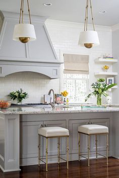 a kitchen with two stools in front of an island and three lights hanging from the ceiling