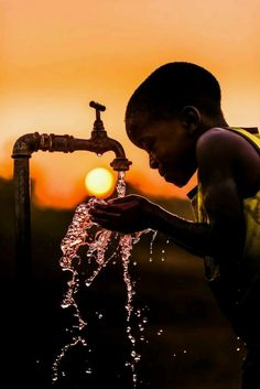 a young boy is drinking water from a faucet in front of the sun