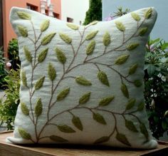 a white pillow with green leaves on it sitting on a wooden box in front of some bushes